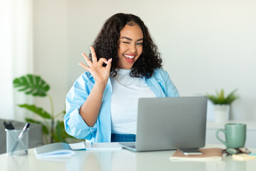 Obraz premium Cheerful Black Businesswoman Using Laptop Gesturing Okay In Modern Office