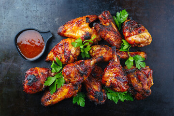 Traditional barbecue chicken wings and drumsticks with hot chili mango sauce and coriander served as top view on a rustic plate with copy space