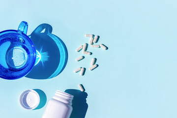 Pills and glass of water on blue background. Medicine, healthcare concept