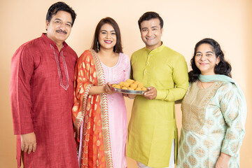 Happy indian family wearing traditional cloths holding plate full of laddu or laddoo sweet...