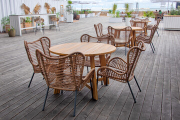 Outdoor cafe with wicker furniture and wooden tables. Empty tables in outdoor sidewalk cafe or restaurant. Touristic setting, cafe table setting