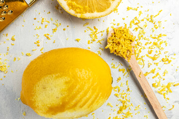 Peeling lemon rind to add zest to Mediterranean recipes. Grater peel and lemon zest on light background, place for text, top view