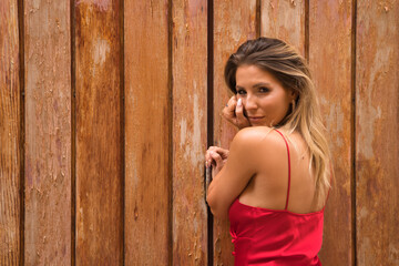 Fototapeta premium Portrait of young, attractive, blonde woman, wearing an elegant red party dress, with sensual look, on a background of wooden planks. Concept beauty, fashion, elegance, luxury, sensuality.