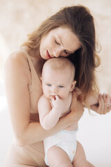 Happy mother in bodysuit sits and embraces her baby.