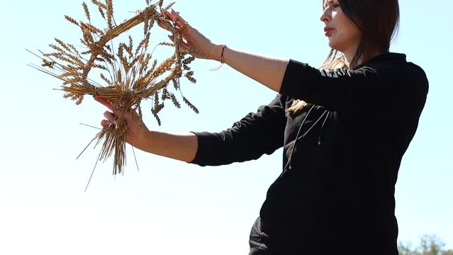 A women holds a wreath of ears of wheat against the background of a golden wheat field. The concept of farming and harvesting in autumn (harvesting wheat, rye, barley) for further flour production