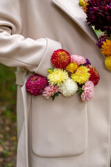 A bouquet of autumn flowers in the pocket of a beige coat