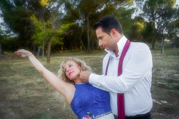 a dance couple rehearses in the garden, the man holds the dancer in his arms caressing her with his hand.