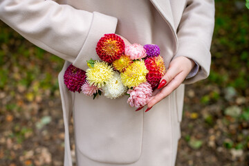 A woman's hand corrects a composition of autumn flowers in the pocket of a beige coat