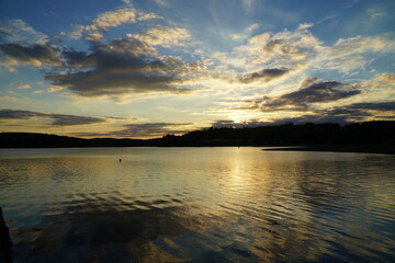 Obraz premium Idyllic evening scene at the Pirk Weischlitz dam in the Vogtland district of Saxony, Germany. Angler on small boat in the backlight of the evening sun on the lake of the dam.