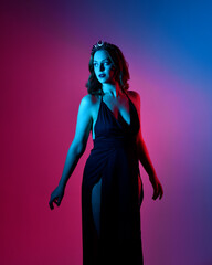 Close up portrait of beautiful woman model wearing elegant black dress and crown, posing against a studio background with fantasy inspired arm gestures, multi coloured creative lighting.