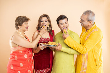 Happy indian family wearing traditional cloths having laddu or laddoo sweet celebration diwali festival together isolated on studio background.