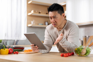 Asian man cooking dinner at home, looking for nice recipe