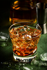 Godfather alcoholic cocktail with scotch whiskey, amaretto liqueur and ice. Dark bar counter background, bar tools, copy space