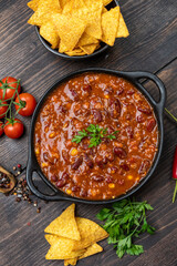 Mexican food chili con carne dish with corn chips nachos on a wooden backdrop. Bean and corn soup, red bean stew
