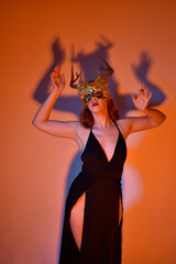 Close up portrait of beautiful woman model wearing elegant black dress, golden horned crown, posing against a studio background with fantasy inspired arm gestures, multi coloured creative lighting.