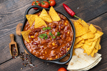 Mexican food chili con carne dish with corn chips nachos on a wooden backdrop. Bean and corn soup,...