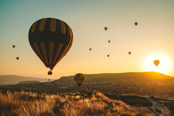 Silhouette of many colorful hot air balloons in sunrise bright sky. Orange sun rise up over Cappadocia Goreme valley landscape. Amazing natural summer morning scenery. Best famous travel location