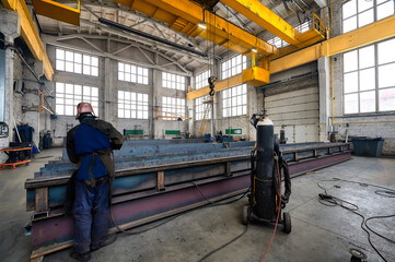 Laborer works with metal details in welding workshop