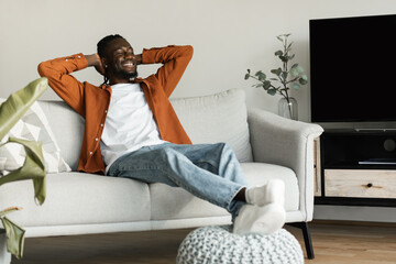 Calm african american man relaxing on couch with hands behind heads at home, enjoying peaceful weekend morning