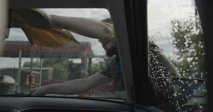 image from inside the car while the worker at the car wash wipes the windows. young man professionally wiping windows with a cloth