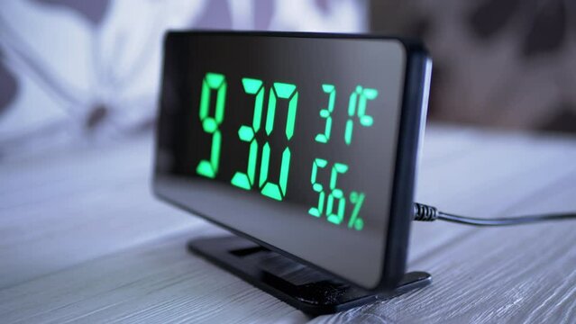 Digital Clock Showing Time on Green Display 9:30 AM, Temperature, Air Humidity. Modern mirror clock, alarm clock with a thermometer, hydrometer standing on a desk on white background. Time concept.