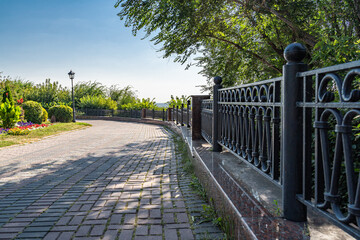 Receding into the distance is a beautiful cast black metal fence along a paving stone path in a city park.