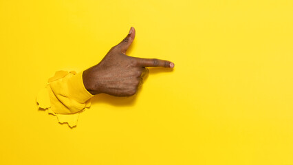 African american male hand pointing aside on virtual object or text, gesturing through the torn yellow paper background