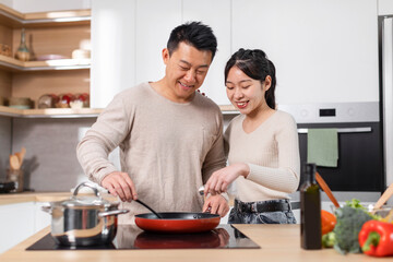 Fototapeta na wymiar Happy chinese husband and wife making dinner together, kitchen interior