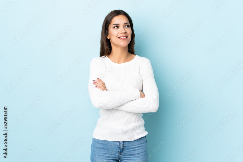 Wall mural Young caucasian woman isolated on blue background looking up while smiling