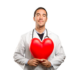 Happy doctor holding a toy heart against white background