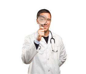 Surprised doctor using a magnifying glass against white background
