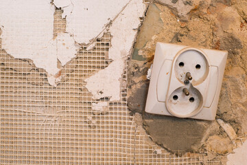 Old power socket on an ancient damaged wall with plaster remnants, brick and plaster mesh. 
Concept of the replacement of electricity in the house and renovation of the flat. Repair work at home