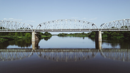 Symmetrical view of the steel truss bridge for trains across the river - obrazy, fototapety, plakaty