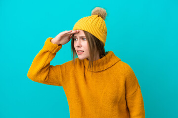 Young English woman wearing winter jacket isolated on blue background looking far away with hand to look something