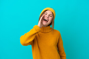 Young English woman wearing winter jacket isolated on blue background shouting with mouth wide open