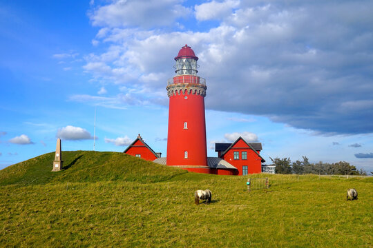 red lighthouse Bovbjerg Fyr illuminated by the light of the setting sun in front of a blue sky with gathering dark clouds in Denmark, near Lemvig, high quality image