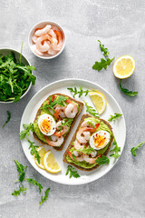 Toast with shrimps, avocado guacamole, arugula and boiled egg, top view