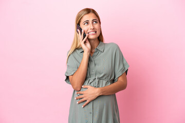 Young Uruguayan woman isolated on blue background pregnant and using mobile phone