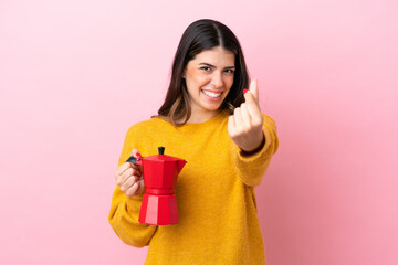 Young Italian woman holding a coffee maker isolated on pink background making money gesture