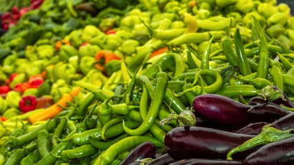 Fresh eggplants are sold at the street market against the background of green fresh peppers
