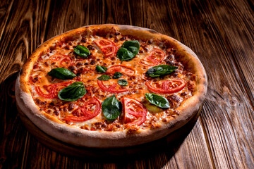 Delicious fragrant pizza with mozzarella, tomatoes and basil with tomato sauce on woden background