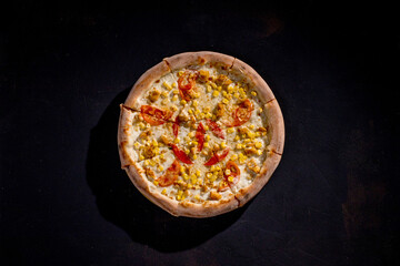 Pizza for children on a cream base with chicken fillet, tomatoes, corn and mozzarella cheese on black background