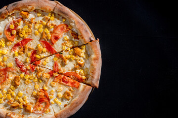 Pizza for children on a cream base with chicken fillet, tomatoes, corn and mozzarella cheese on black background