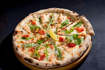 Pizza with salmon, mozzarella, cherry tomatoes, arugula, lemon and parmesan. Italian cuisine