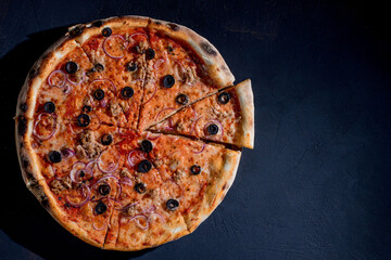 Pizza with tuna, olives, onions, mozzarella cheese and tomato sauce on a black background. Top view