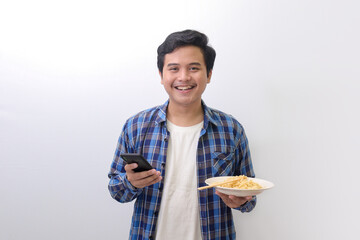 Portrait of happy Asian man in blue plaid shirt eating delicious instant noodles with chopsticks...