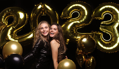 Happy gorgeous girls in stylish sexy party dresses holding gold 2023 balloons, having fun at New Year's Eve Party. - obrazy, fototapety, plakaty