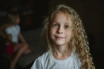 close-up portrait of a little girl against the background of her sister sitting on the sofa in a sad pose. Jealousy between children