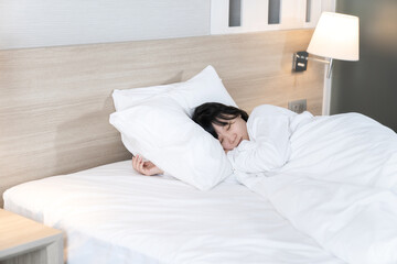 Asian cute young woman in white long arm pajamas lie on her side on the bed