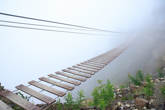 Fototapeta Hanging rope bridge vanishing in fog. Tourist suspension bridge. No people